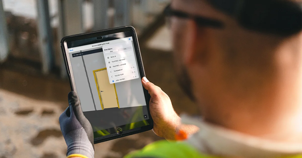 Construction worker using Fieldwire on iPad in the field, viewing a 3D BIM model with door and dimension callouts visible on the tablet screen